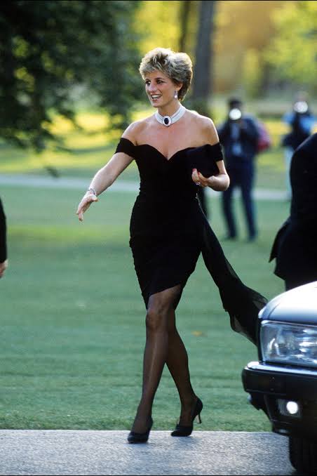 Princess Diana walks confidently in a fitted black off-the-shoulder dress after stepping away from a car.