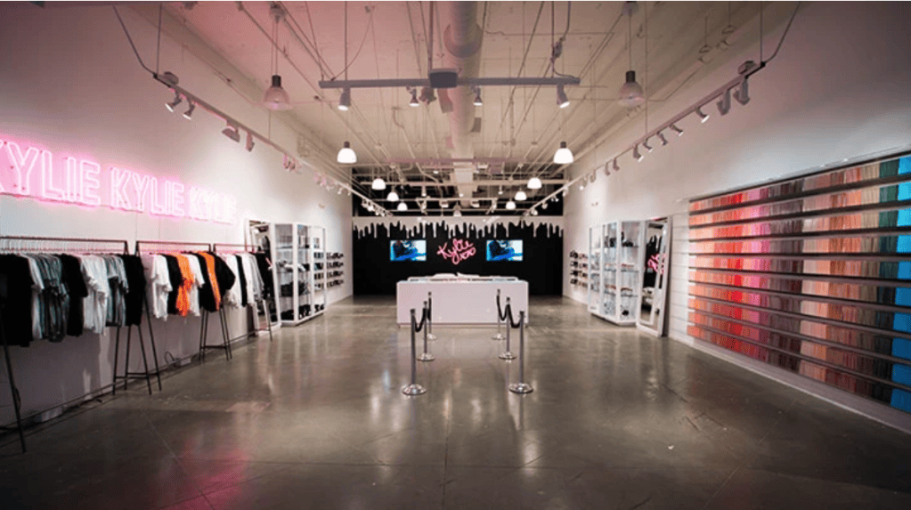 Kylie Cosmetics pop-up shop featuring a neon Kylie sign, clothing displays, product shelves, and a wall filled with colorful Lip Kits.