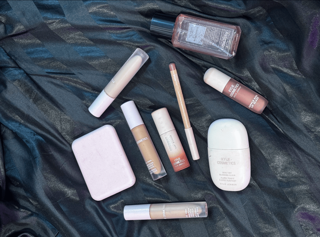 Kylie Cosmetics products in pink and nude packaging arranged across textured black fabric.